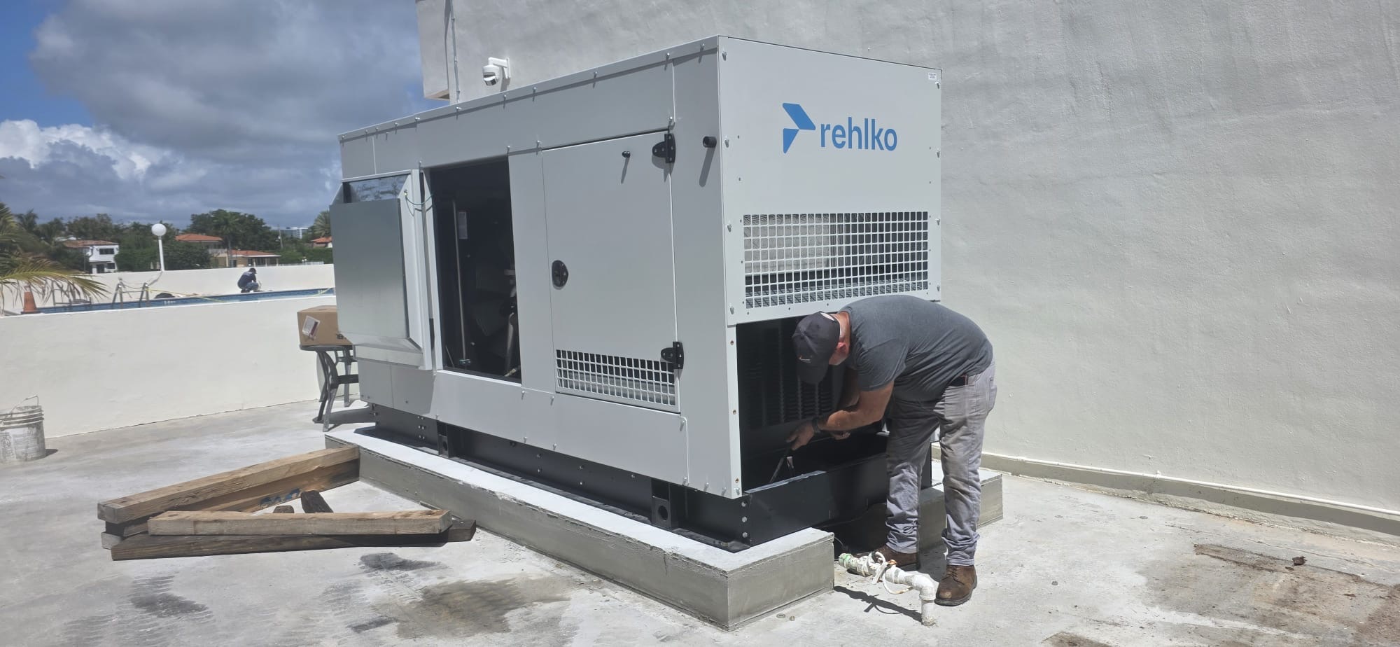 Technician working beside a large Rehlko generator on a concrete support base.