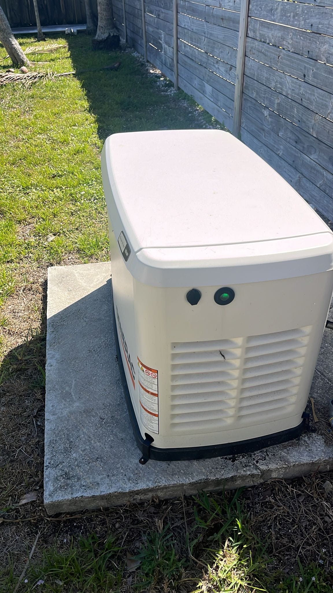 Residential standby generator on a concrete pad beside a yard.